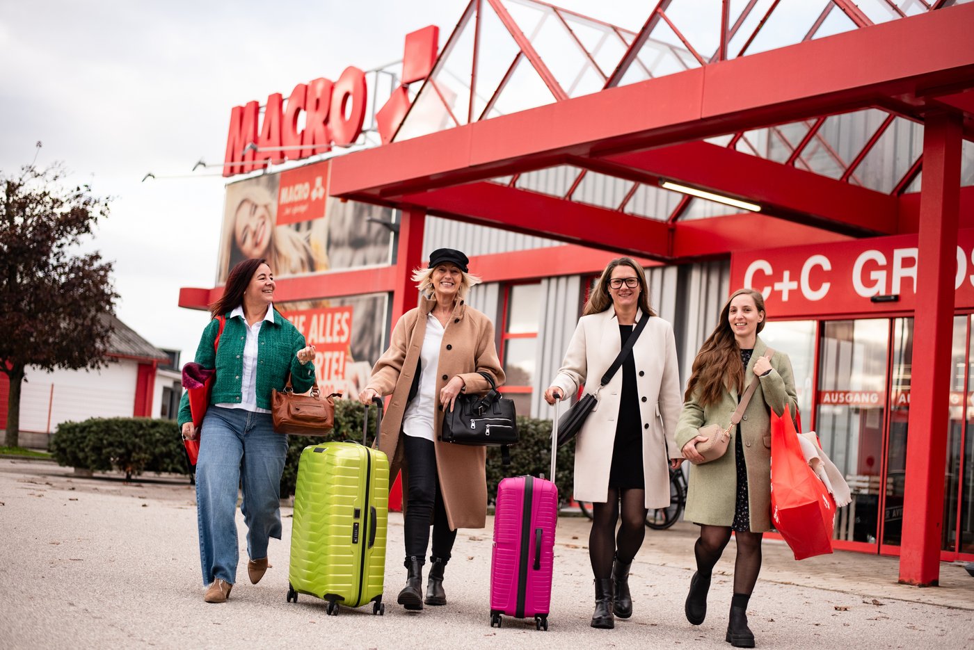 Vier Frauen vor einem Macro C+C Großhandel, zwei mit Rollkoffern.